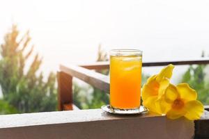 verre de jus d'orange avec fleur jaune sur balcon avec des gouttes de pluie le matin