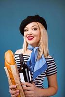 portrait d'une belle femme française blonde en béret, écharpe, dos et chemise blanche, avec bouteille de vin et baguette de pain dans ses bras avec drapeau français sur fond photo