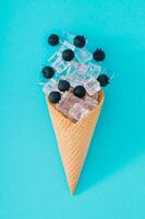 la glace crème cône avec myrtilles et la glace cubes sur aqua bleu Contexte. minimal été Créatif mise en page. fruit et bonbons concept. été sucré nourriture esthétique. plat poser. photo