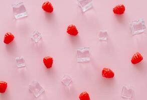 Créatif été modèle fabriqué de framboises et la glace cubes sur lumière rose Contexte. fruit minimal concept. branché en bonne santé nourriture modèle Contexte idée. plat poser. photo