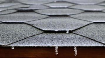 toiture sur le toit d'une maison ou d'un belvédère en tuiles bitumineuses avec de l'eau courante gelée et des glaçons suspendus. fermer. photo