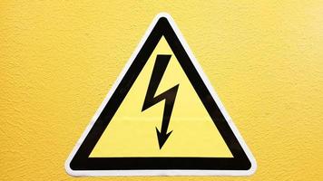 panneau de sécurité jaune et noir collé sur un mur jaune. foudre à haute tension dans un triangle attention attention danger électricité mort. photo