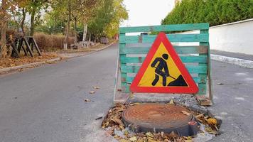 réparation de routes. regard d'égout sur la chaussée. Les conducteurs de voitures d'avertissement triangulaires signent avec un homme avec une pelle jaune avec du rouge. Hommes au travail. panneaux de signalisation, restrictions de voyage. photo