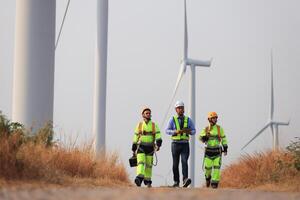 spécialiste vent turbine équipe de ingénieurs discuter vert énergie production dans vent turbines ferme ou Moulins à vent champ. équipe de ingénieur énergie Planification activité dans Moulins à vent industriel zone photo