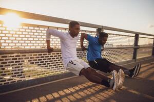 deux Afro-américain copains sont exercice sur le pont dans le ville. elles ou ils sont Faire sens inverse des pompes. photo