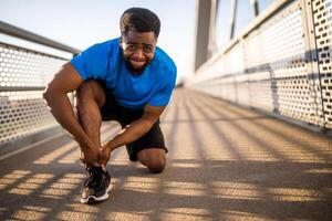 Jeune Afro-américain homme est blessé tandis que jogging. il tordu le sien cheville. photo