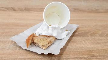 les restes de nourriture sur une assiette en papier et une tasse de café en papier sale vide sur une table en bois dans un café de restauration rapide photo