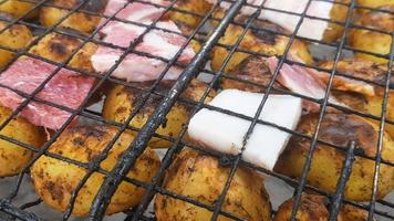 pommes de terre grillées au bacon, entières cuites sur le gril du barbecue. mise au point sélective. petites pommes de terre entières avec des morceaux de bacon et grillées. pommes de terre au four avec bacon grillé. photo