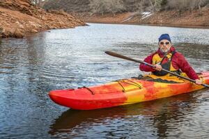 Sénior Masculin pagayeur est pagayer coloré rivière kayak sur une calme Lac - des loisirs concept, du froid saison sur dent de cheval réservoir dans Colorado photo