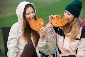 deux Jeune femmes dans chaud vêtements ayant amusement et en mangeant biscuits dans le parc photo