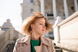 une femme avec longue cheveux est permanent sur une ensemble de escaliers. elle est portant une vert chemise et une bronzer manteau. photo