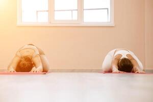 deux magnifique femmes faire yoga, des sports dans le salle de sport. le concept de la grâce et beauté de le corps. photo