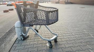 chariot d'épicerie vide en plein air près du supermarché. solitude, isolement du chariot, quarantaine, coronavirus. un panier en plastique vide sur roues avec des pièces en plastique jaune laissées sur le trottoir près du magasin. photo