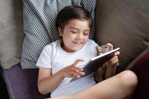 enfant Faire devoirs avec numérique tablette dans vivant chambre, enfant en utilisant gadgets à étude.école garçon apprend en ligne de maison, éducation apprentissage avec Nouveau La technologie pour enfants. photo