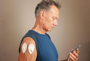 homme en utilisant un électro thérapie masseur ou dizaines unité sur le sien deltoïdes pour douleur le soulagement pour muscles et les articulations photo