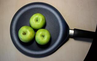 Trois mûr vert juteux pommes dans une friture la poêle sur en bois table photo