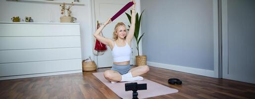 portrait de souriant Jeune femme, création contenu pour aptitude Blog, enregistrement pendant faire des exercices avec la résistance groupe, séance sur yoga tapis photo