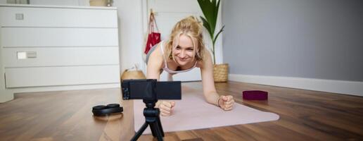 portrait de Jeune sportif vlogger, aptitude instructeur permanent dans planche sur caoutchouc yoga tapis, enregistrement de se Faire faire des exercices à Accueil photo