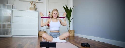 portrait de Jeune athlétique femme enregistrement Accueil faire des exercices , tournage contenu pour sport aptitude vlog, en utilisant la résistance bande et numérique caméra photo