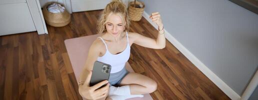 Jeune sportif aptitude entraîneur, yoga instructeur Est-ce que vivre flux, prend selfies sur téléphone intelligent tandis que séance sur caoutchouc tapis à maison, enregistrement sa faire des exercices formation session photo