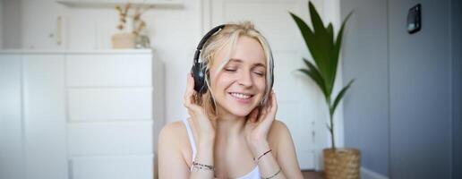 concept de gens et mode de vie, proche en haut de magnifique blond femme dans sans fil écouteurs, écoute à musique, jouit bien qualité du son dans Nouveau écouteurs photo