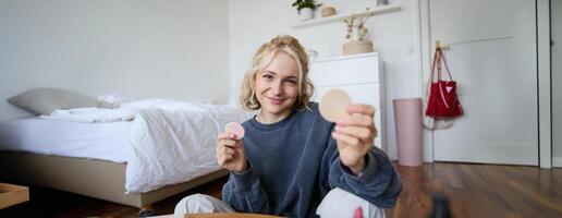 portrait de Jeune femme, contenu créateur, montrant beauté maquillage des produits à caméra, séance sur sol dans chambre et souriant photo