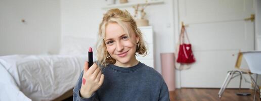 portrait de souriant blond femme, enregistrement , en ligne vivre courant à propos beauté des produits, contenu fabricant les taux sa maquillage des produits, spectacles rouge à lèvres sur caméra photo