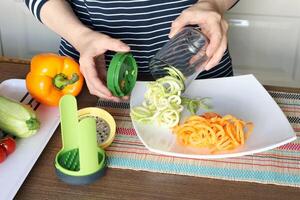 femme tire tranché des légumes de récipient de légume hachoir dans cuisine. photo