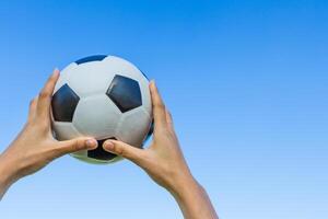 fille main détient une football Balle dans le ciel sur bleu ciel Contexte. photo