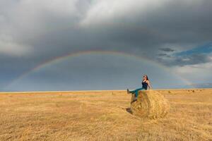 magnifique Jeune fille dans une champ avec paille sur une Contexte de arc en ciel photo