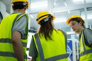 retour vue de groupe Jeune usine ouvrier portant une difficile chapeau à la recherche à une ordinateur écran utilisé à contrôle production. photo