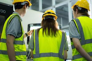 retour vue de groupe Jeune usine ouvrier portant une difficile chapeau à la recherche à une ordinateur écran utilisé à contrôle production. photo