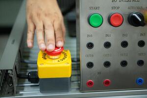 fermer de main pressage le Arrêtez bouton sur le contrôle panneau de un industriel machine. photo