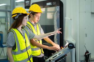 tous les deux de Jeune usine ouvrier portant une difficile chapeau à la recherche à une ordinateur écran utilisé à contrôle production. photo