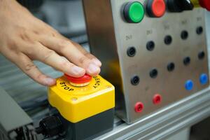 fermer de main pressage le Arrêtez bouton sur le contrôle panneau de un industriel machine. photo