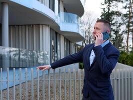 une homme d'affaire engage dans une téléphone conversation à l'extérieur un Bureau bâtiment, habillé dans formel affaires tenue. le homme d'affaires professionnel comportement est évident comme il discute important questions. photo