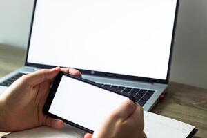 homme détient mobile téléphone à le table dans de face de ordinateur portable, Vide écrans photo