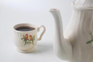 proche en haut photo de une tasse de sucré thé et une blanc théière avec céramique Matériel