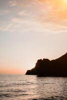 une rouge brûlant le coucher du soleil plus de le mer avec rocheux volcanique falaise. abstrait la nature été ou printemps océan mer Contexte. photo