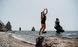 femme été Voyage mer. content touristique dans chapeau prendre plaisir prise image en plein air pour souvenirs. femme voyageur posant sur le plage à mer entouré par volcanique montagnes, partage Voyage aventure périple photo