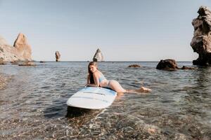 femme mer souper. proche en haut portrait de content Jeune caucasien femme avec longue cheveux à la recherche à caméra et souriant. mignonne femme portrait dans une bleu bikini posant sur souper planche dans le mer photo