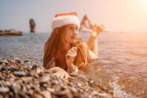 femme Voyage mer. content touristique prendre plaisir prise image sur le plage pour souvenirs. femme voyageur dans Père Noël chapeau regards à caméra sur le mer baie, partage Voyage aventure périple photo