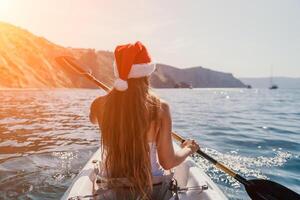 femme dans kayak retour voir. content Jeune femme dans Père Noël chapeau flottant dans kayak sur calme mer. été vacances vacances et de bonne humeur femelle gens relaxant ayant amusement sur le bateau. photo