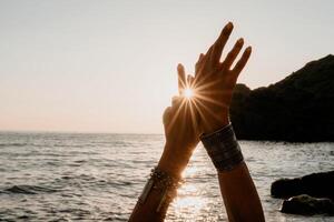 femme mer yoga. content femme dans blanc maillot de bain et boho style bracelets pratiquant en plein air sur yoga tapis par mer sur le coucher du soleil. femmes yoga aptitude routine. en bonne santé mode de vie, harmonie et méditation photo