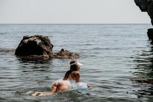 femme été mer. content femme nager avec gonflable Donut sur le plage dans été ensoleillé jour, entouré par volcanique montagnes. été vacances concept. photo