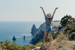 femme Voyage mer. content touristique dans chapeau prendre plaisir prise image en plein air pour souvenirs. femme voyageur posant sur le plage à mer entouré par volcanique montagnes, partage Voyage aventure périple photo