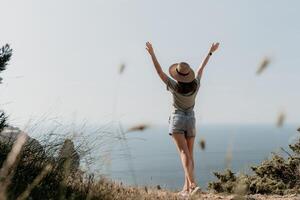 femme Voyage mer. content touristique dans chapeau prendre plaisir prise image en plein air pour souvenirs. femme voyageur posant sur le plage à mer entouré par volcanique montagnes, partage Voyage aventure périple photo