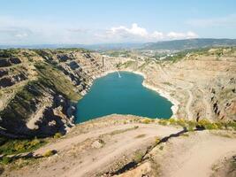 aérien Haut vue sur à ciel ouvert exploitation minière carrière avec inondé bas, turquoise surface de le lac. carrière étang trop développé avec vert les plantes et clair turquoise l'eau photo