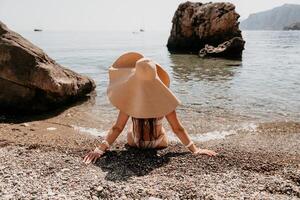 femme Voyage mer. content touristique dans chapeau prendre plaisir prise image en plein air pour souvenirs. femme voyageur posant sur le plage à mer entouré par volcanique montagnes, partage Voyage aventure périple photo