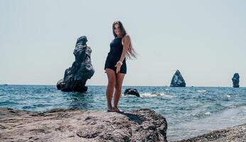 femme été Voyage mer. content touristique dans chapeau prendre plaisir prise image en plein air pour souvenirs. femme voyageur posant sur le plage à mer entouré par volcanique montagnes, partage Voyage aventure périple photo